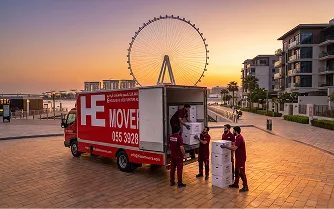 E House Mover truck with moving team at Dubai waterfront during sunset.