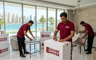 Movers packing furniture and boxes inside a Dubai apartment with sea view.